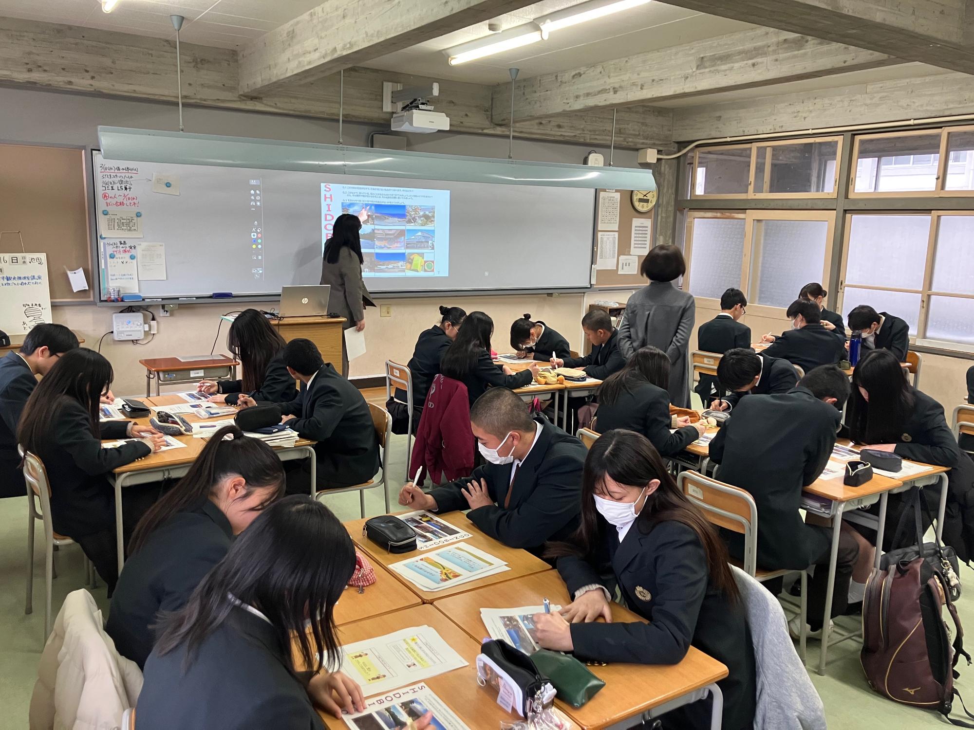 志度高校にてビンゴゲームの答え合わせを行う生徒と教団の女性の写真