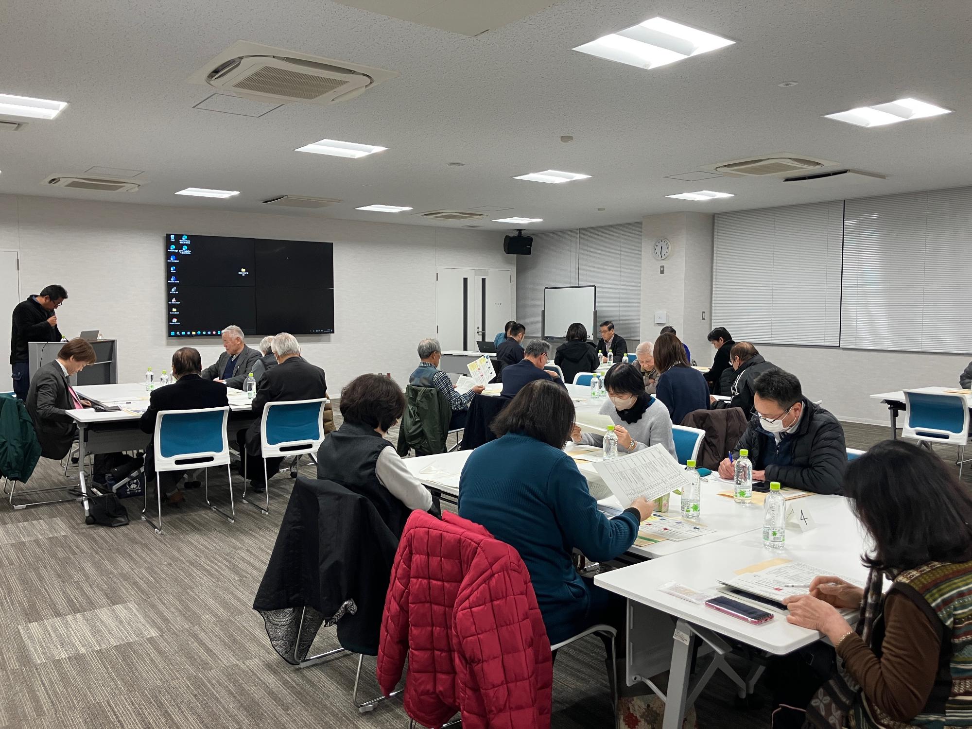 会議室にて瀬戸内国際芸術祭2025の報告を行う事務局男性と報告を聞く参加者の写真