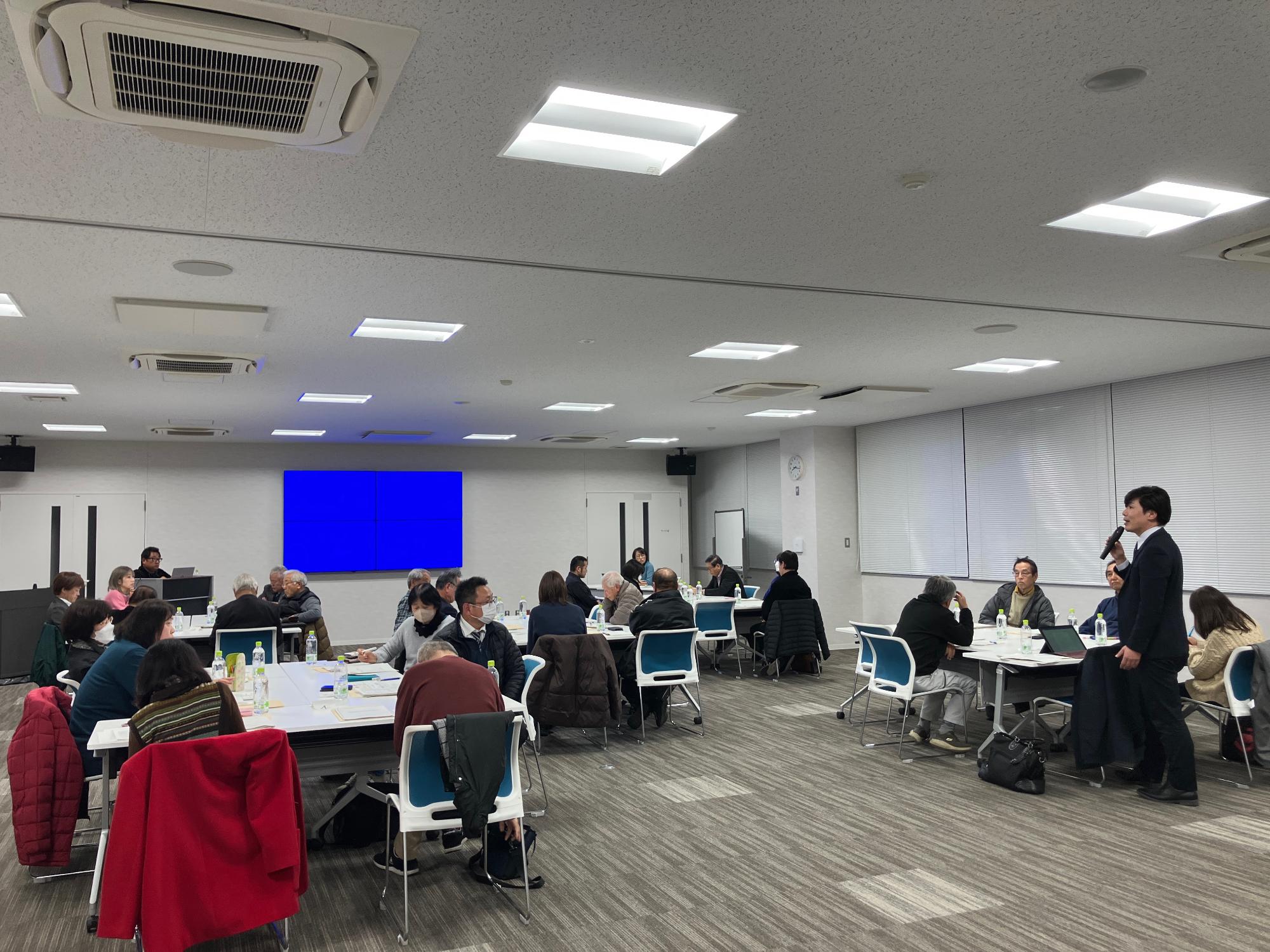 会議室にてグループワークで出た意見を発表する男性の写真