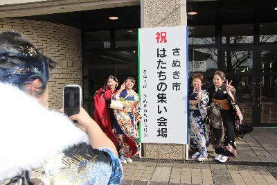 はたちの集いの立て看板の左右でピースする4名の振り袖姿の女性その様子をスマート