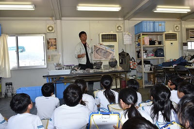 県埋蔵文化財センターの職員が竪穴式住居について説明し、児童たちが聞いている様子