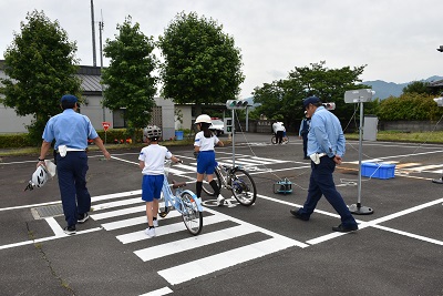 自転車を押して歩く2人の児童と、2人の男性警察官