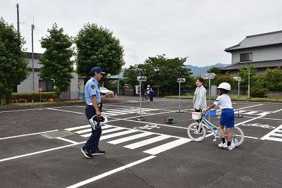 男性警察官と女性職員に見守られながら、自転車を押して歩く児童