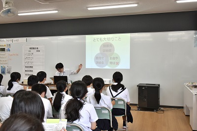 教室で市選管の職員が説明し、スクリーンを見ながら授業を受ける児童たち