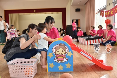 すべり台にボールを置く子どもと、それを見守る保護者と先生