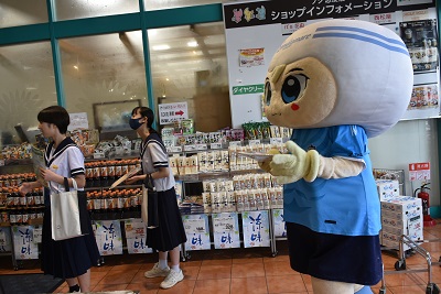 店内で来店客へ声をかける中学生2名と、カマタマーレ讃岐のマスコットキャラクター「さぬぴー」