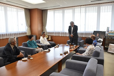 椅子に座る選手4名と市グラウンド・ゴルフ会長が、立って話す市長の激励を聞いている様子