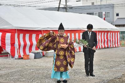 宮司とスーツ姿の男性が建築予定地の四隅で細かく切った紙をまき、清める様子