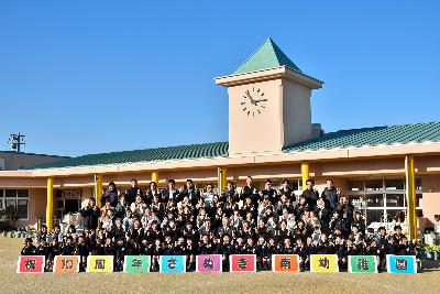 さぬき南幼稚園の園庭で建物をバックに園児や保護者、関係者全員で記念撮影をする様子