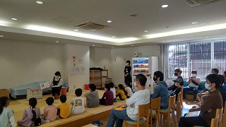 男女共同参画セミナーで子どもたちに「おさるのジョージとしょかんへいく」の読み聞かせをしている様子の写真