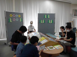 「えほんのもり」と書かれた衝立のコーナーでお父さんが子どもに読み聞かせをしている様子の写真