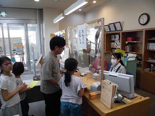 図書館内に設置された「たんていじむしょ」で謎解きゲームに関する説明を受けている様子の写真