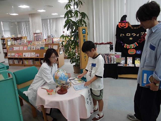 地球儀が置かれたテーブルで本を広げ謎解きゲームをしている子どもとそれを見守るお父さんの写真