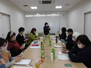 会議室で参加者が長いテーブルに座り講師の話を聞いている写真