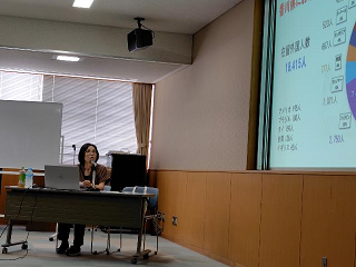 スクリーンに大きく映し出された資料を講師が説明している写真