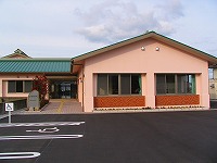 駐車場とスロープが整備されたピンク色の外壁と緑色の屋根の辛立文化センターの外観写真