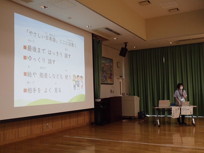 女性講師がスクリーンの横に立ち講演を行っている写真