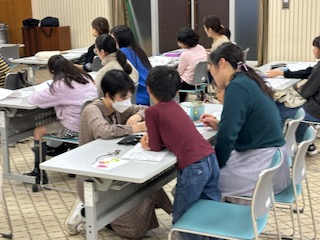 ドイツ語学習で直接机に来て教えてくれている講師とその説明を一緒に聞く親子の写真