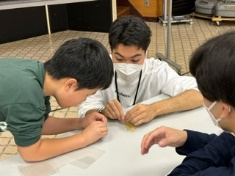 講師に教えてもらいながらキーホルダー作りを進める児童の写真