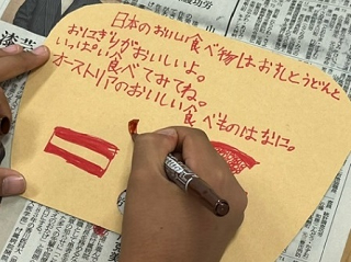 オーストリアの市民に向けて児童がうちわ型の手紙に「オーストラリアのおいしい食べものはなに？」と質問を書いている写真