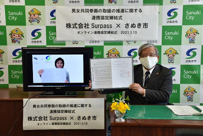 締結された男女共同参画の取組の推進に関する協定書を広げて見せるさぬき市長の写真