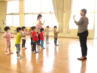 ホールで先生の前に並んだ子どもたちが手を振って挨拶している様子の写真