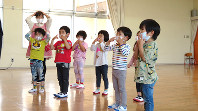 ホールで子どもたちが頭や頬に手を当てながら英語の歌遊びをしている様子の写真