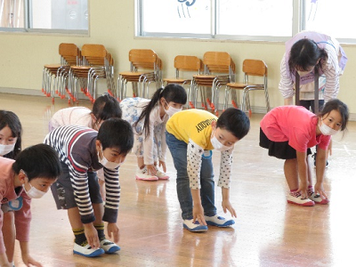 ホールで子供たちが前屈の姿勢で体を伸ばしている写真