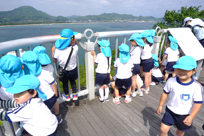 海の見える展望台で子どもたちが望遠鏡や手すりから景色を眺めている様子の写真