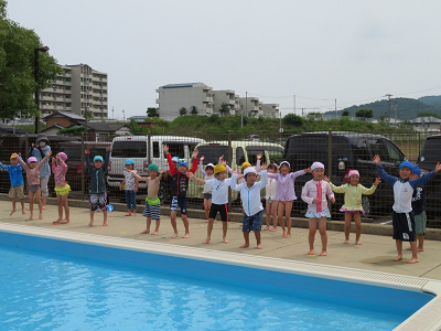 プールサイドで子どもたちが体操をして準備運動をしている様子の写真