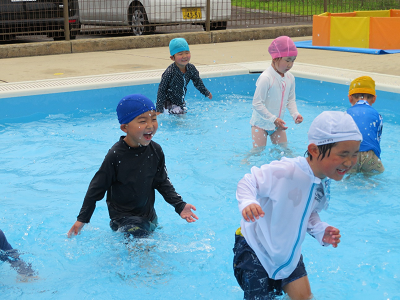 プールの中を走り回り、子どもたちが笑顔で鬼ごっこを楽しんでいる様子の写真