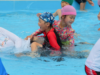 ワニになった先生の背中に乗り笑顔で楽しんでいる2人の子供の写真