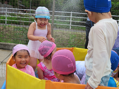 カラフルなビニールプールに入り、笑顔で水遊びを楽しむ子供たちの写真