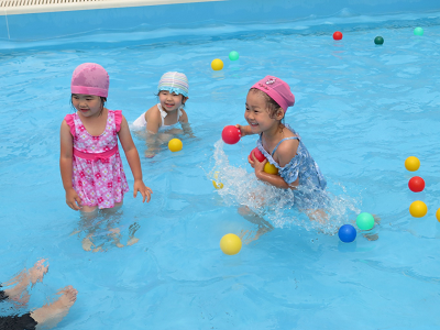 プールに浮かんだボールを胸に抱えて笑顔で走っている女の子とプールに立っている2人の女の子の写真