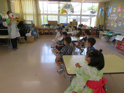 室内で椅子に座って先生の話を聞く浴衣姿の園児たちの写真