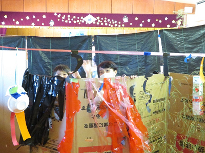 屋内に設置された手作りの屋台セットから顔を出す2人の大人の写真