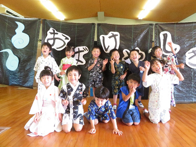 大きな文字でお化けやしきと書かれた黒い垂れ幕の前で様々なポーズをとる園児たちの写真