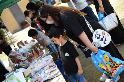 屋外の机に商品が並べられ商品を吟味する園児と保護者の写真