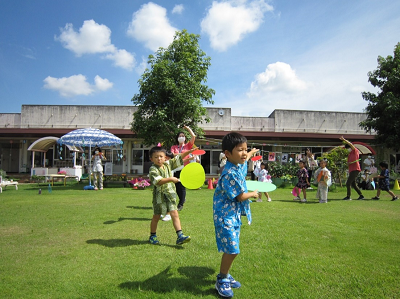 芝生の上でうちわを持って様々なポーズをとって踊る園児たちの写真