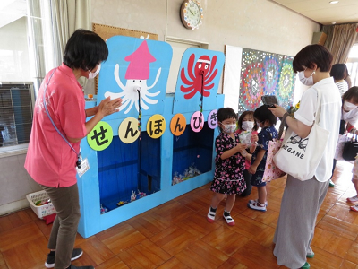 屋内で保護者と一緒にせんぼんびきゲームを楽しむ園児たちの写真