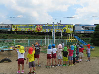 校庭の脇を通過するアンパンマン列車に横一列に並び元気に手を振る子どもたちの写真
