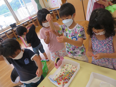カラフルなビーズを白い糸に真剣な表情で通している子どもたちの写真