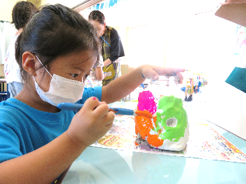 集中した様子で、紙粘土を貼り付けたビンに色を塗る女の子の写真