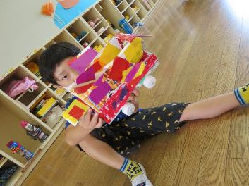 赤や黄色のカラフルなビニールテープで装飾された手作りの車を両手で持っている男の子の写真