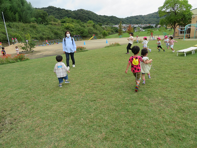 園庭の芝生で保育者と一緒に遊ぶ子どもたちの写真