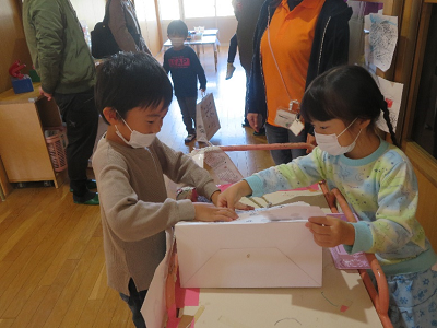 室内の工作テーブルで子供たちが紙工作を一緒に作っている写真