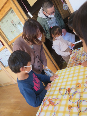 室内の工作テーブルで保護者と子供が輪飾り作りをしている写真