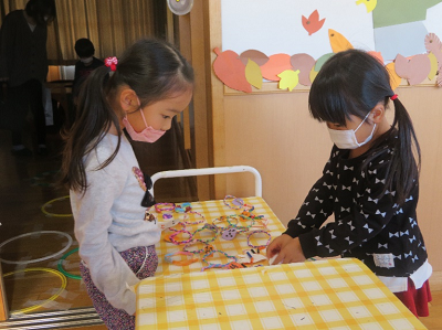 室内の工作テーブルで女の子たちが輪飾りを並べて作っている写真
