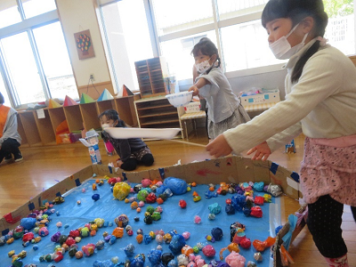 室内の遊び場で子供たちが段ボールの囲いの中でカラフルなボール遊びをしている写真
