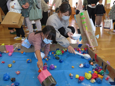 室内の段ボールの囲いの中で保護者と子供がカラフルなボールを拾っている写真